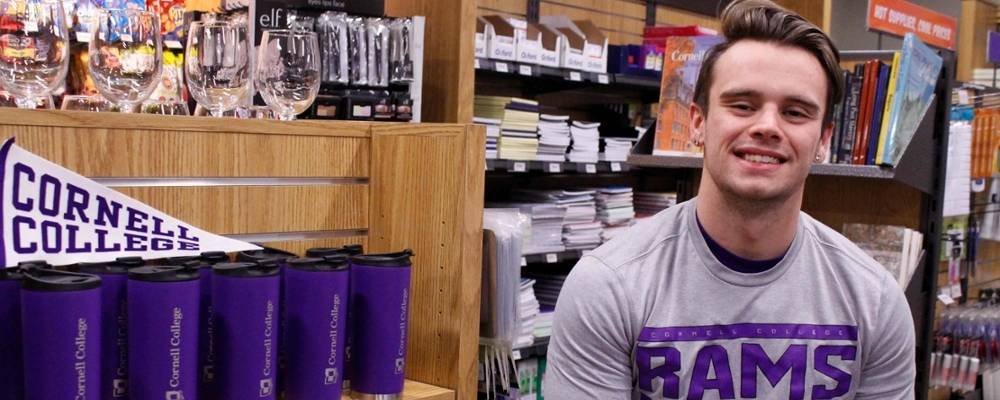 Cornell student wears a Cornell t-shirt inside the bookstore next to Cornell gear. 