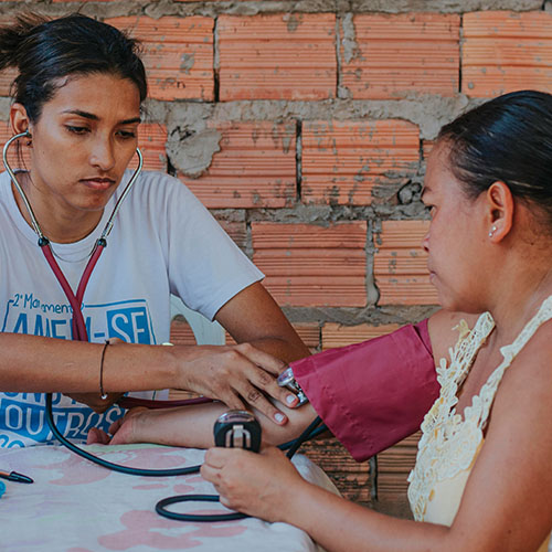 Woman taking a blood pressure reading for another woman, photo credit Carlos Magno, Unsplash