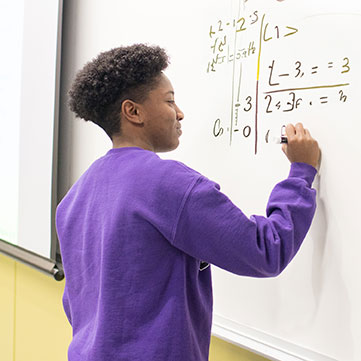 student working a math problem at the whiteboard