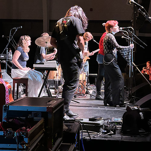 View of a rock band performing from the sidelines behind audio equipment..