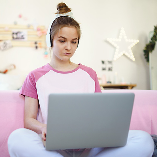 Teen with a laptop sitting on a couch.