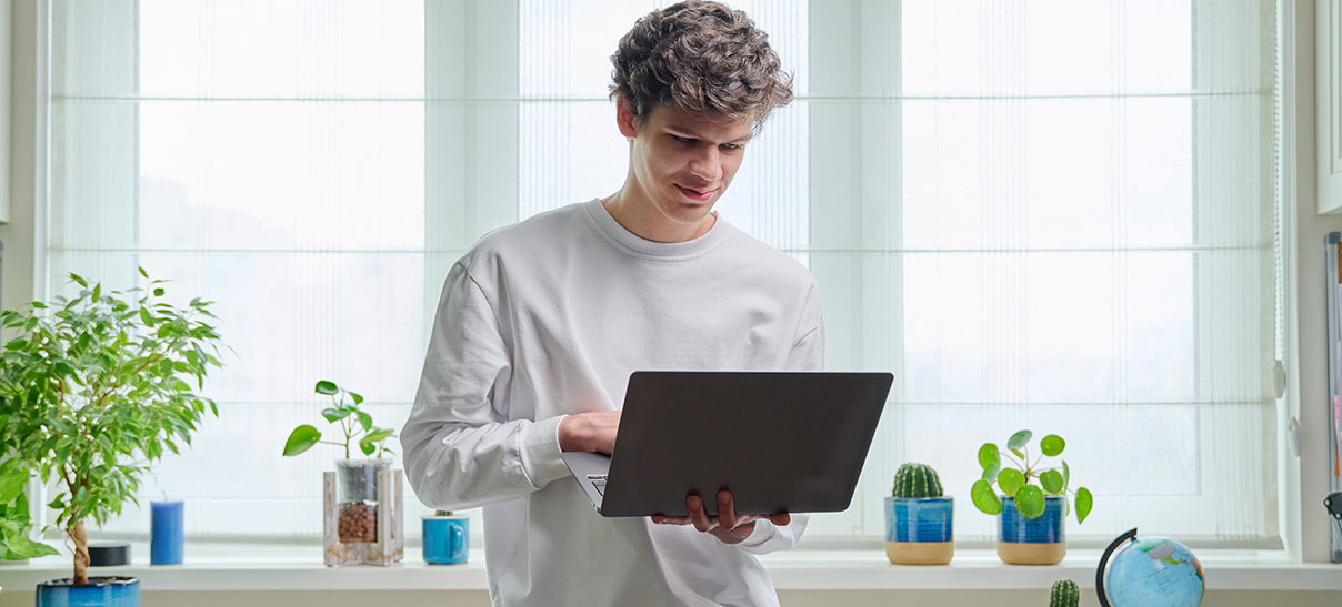 Teen carries a laptop as he's working on it.