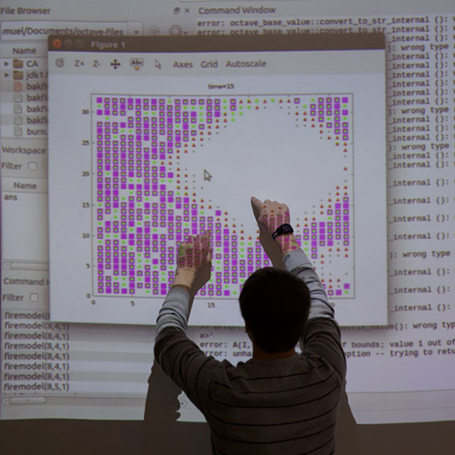 Students and professor examine snake specimen in a meadow.